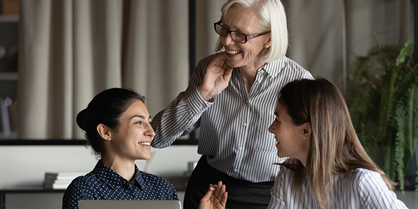 Business women talking at workplace with laptop, having fun, sharing good news, enjoying working together